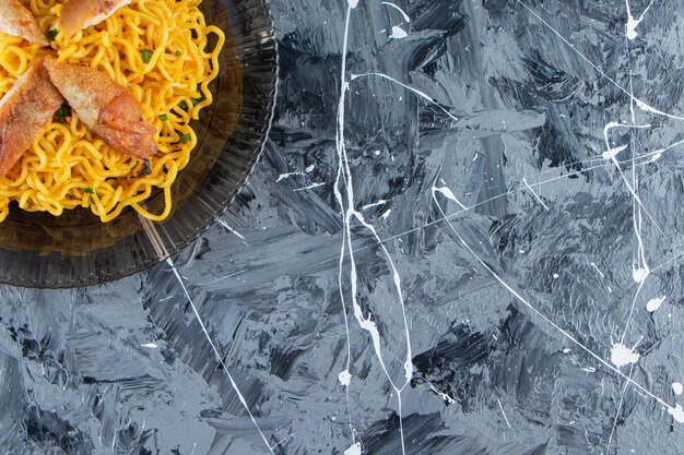 Fideos cocidos en un plato de cristal, sobre el fondo de mármol.