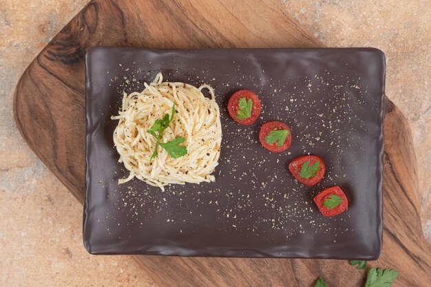 Fideos con especias y tomates en placa negra.