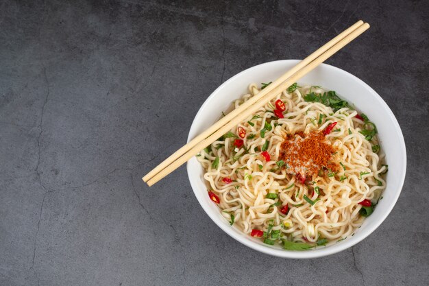 Fideos instantáneos listos para comer con palillos en la taza en la pared negra.