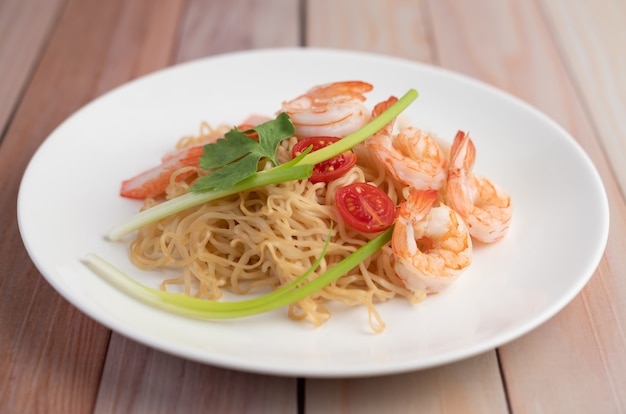 Fideos instantáneos salteados con langostinos y palitos de cangrejo en un plato blanco.