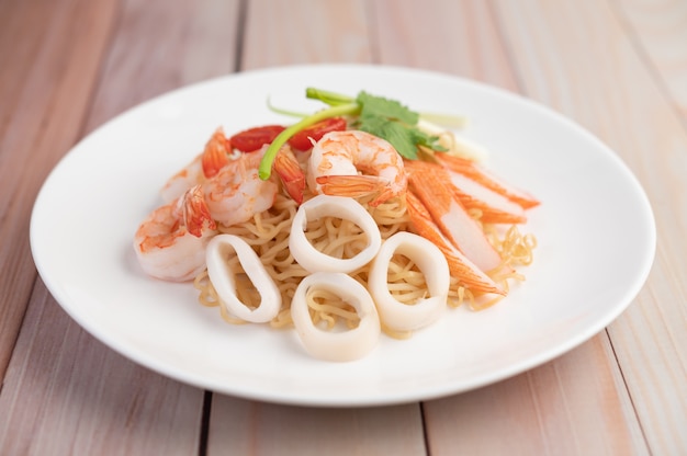 Fideos instantáneos salteados con langostinos y palitos de cangrejo en un plato blanco.