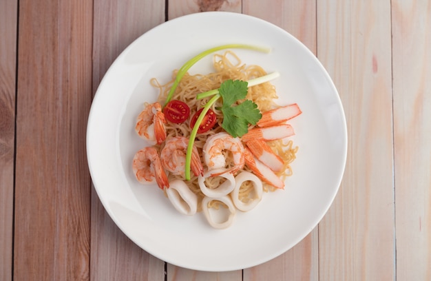 Fideos instantáneos salteados con langostinos y palitos de cangrejo en un plato blanco.