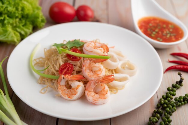 Fideos instantáneos salteados con langostinos y palitos de cangrejo en un plato blanco.