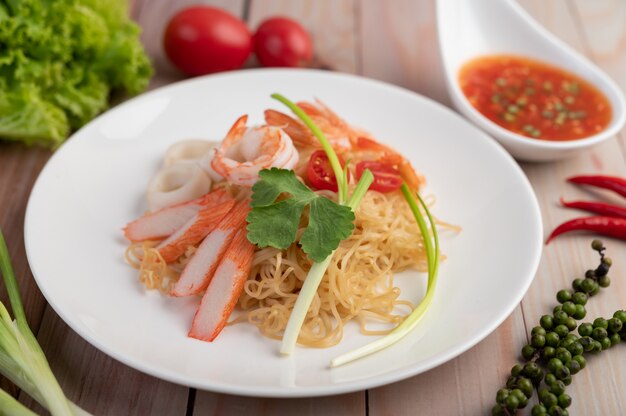 Fideos instantáneos salteados con langostinos y palitos de cangrejo en un plato blanco.