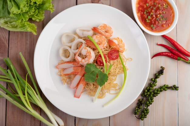 Fideos instantáneos salteados con langostinos y palitos de cangrejo en un plato blanco.