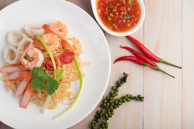 Fideos instantáneos salteados con langostinos y palitos de cangrejo en un plato blanco.