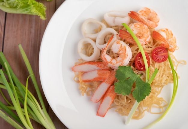 Fideos instantáneos salteados con langostinos y palitos de cangrejo en un plato blanco.