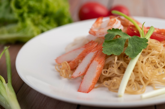 Fideos instantáneos salteados con langostinos y palitos de cangrejo en un plato blanco.