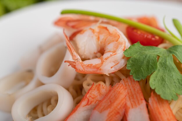 Fideos instantáneos salteados con langostinos y palitos de cangrejo en un plato blanco.