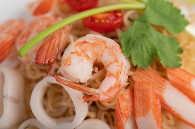 Fideos instantáneos salteados con langostinos y palitos de cangrejo en un plato blanco.