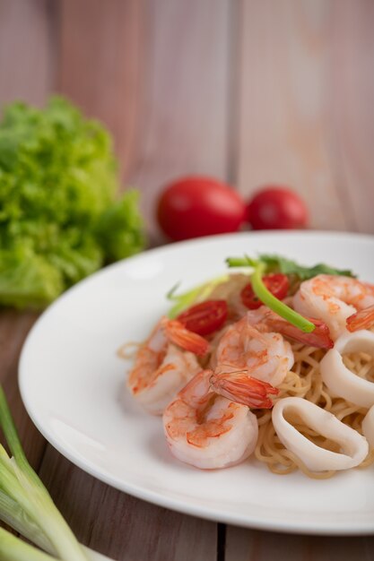 Fideos instantáneos salteados con langostinos y palitos de cangrejo en un plato blanco.