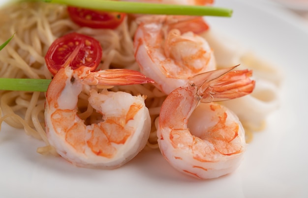 Fideos instantáneos salteados con langostinos y palitos de cangrejo en un plato blanco.