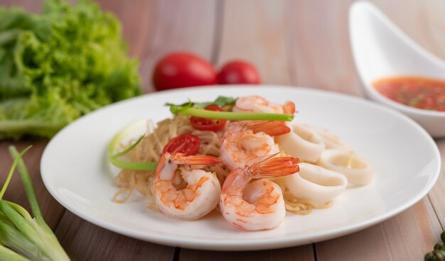 Fideos instantáneos salteados con langostinos y palitos de cangrejo en un plato blanco.