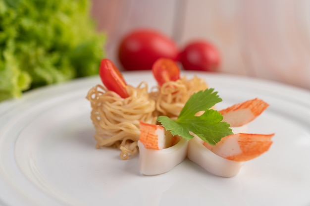 Fideos instantáneos salteados con langostinos y palitos de cangrejo en un plato blanco.