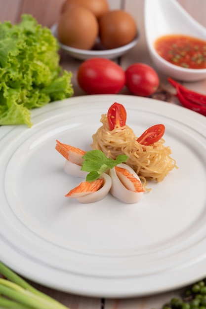 Fideos instantáneos salteados con langostinos y palitos de cangrejo en un plato blanco.