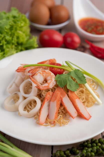 Fideos instantáneos salteados con langostinos y palitos de cangrejo en un plato blanco.