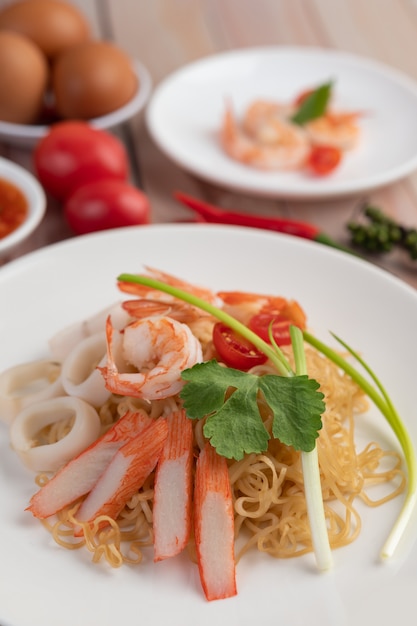 Fideos instantáneos salteados con langostinos y palitos de cangrejo en un plato blanco.