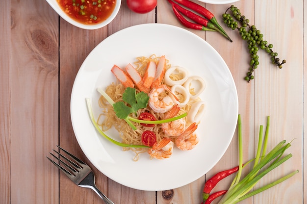 Fideos instantáneos salteados con langostinos y palitos de cangrejo en un plato blanco.