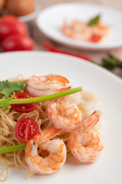 Fideos instantáneos salteados con langostinos y palitos de cangrejo en un plato blanco.