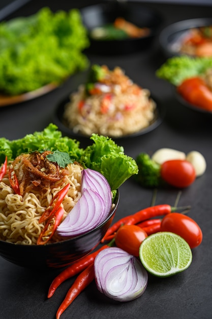 Fideos picantes en el bol con ingredientes sobre superficie de cemento negro