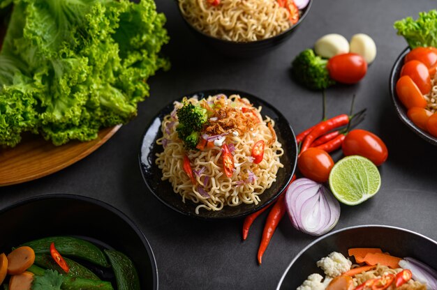 Fideos picantes en el bol con ingredientes sobre superficie de cemento negro