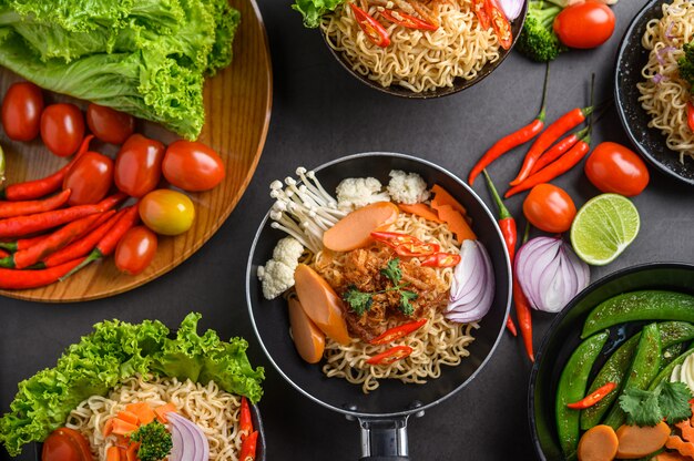 Fideos picantes en las sartenes con ingredientes en la superficie de cemento negro, vista superior.