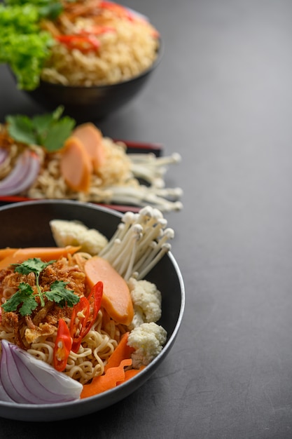 Fideos picantes en las sartenes con ingredientes en la superficie de cemento negro.