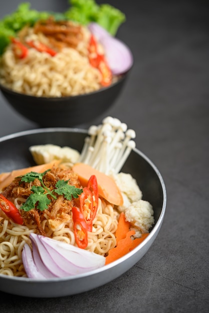 Fideos picantes en las sartenes con ingredientes en la superficie de cemento negro.