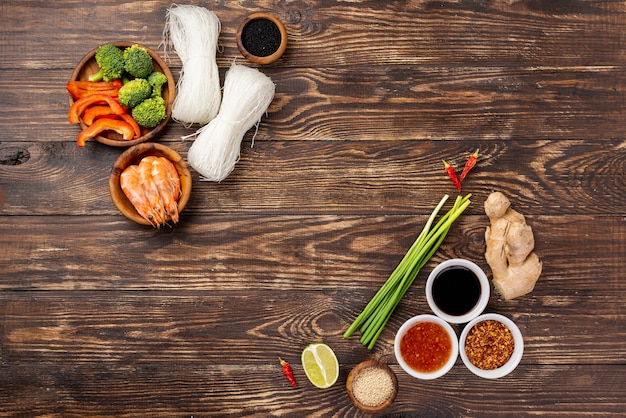 Fideos planos, especias y palillos sobre fondo de madera