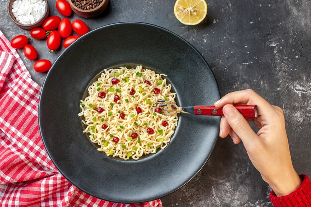 Fideos ramen de vista superior en placa negra con tenedor en mano de mujer sobre mesa oscura