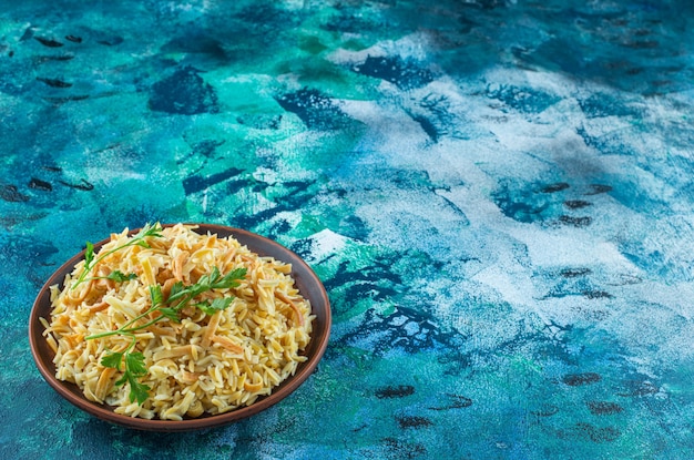 Fideos sabrosos caseros en un cuenco, sobre la mesa azul.