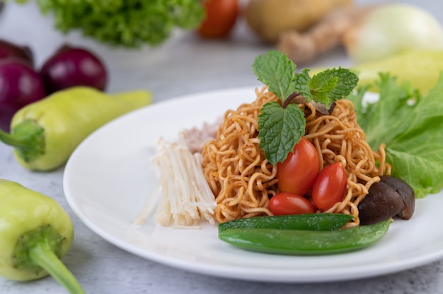 Fideos salteados con carne picada de cerdo, edamame, tomates y champiñones en un plato blanco.