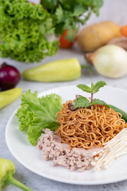 Fideos salteados con carne picada de cerdo, edamame, tomates y champiñones en un plato blanco.