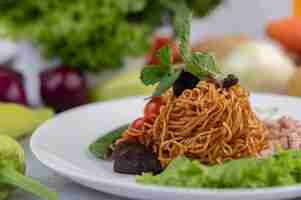 Foto gratuita fideos salteados con carne picada de cerdo, edamame, tomates y champiñones en un plato blanco.