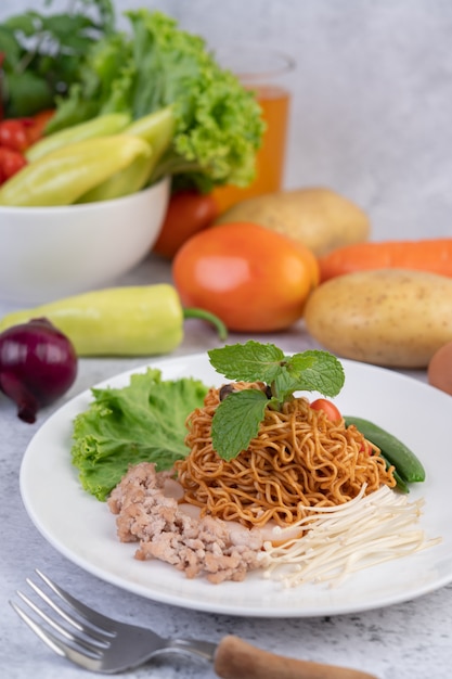 Fideos salteados con carne picada de cerdo, edamame, tomates y champiñones en un plato blanco.