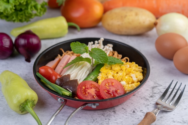 Fideos salteados que combinan maíz, setas con agujas doradas, tomate, salchichas, edamame y cebolletas en una sartén.