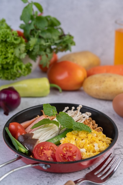 Fideos salteados que combinan maíz, setas con agujas doradas, tomate, salchichas, edamame y cebolletas en una sartén.