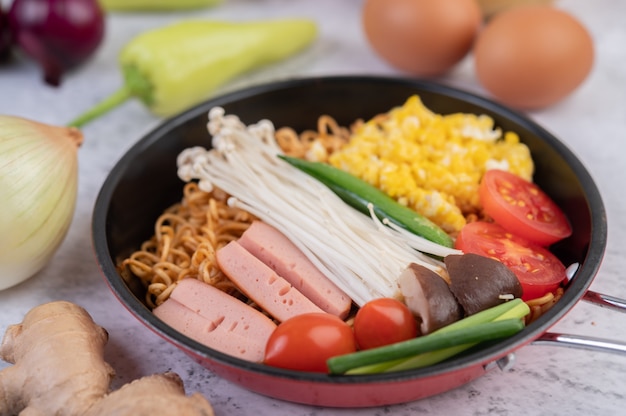 Fideos salteados que combinan maíz, setas con agujas doradas, tomate, salchichas, edamame y cebolletas en una sartén.