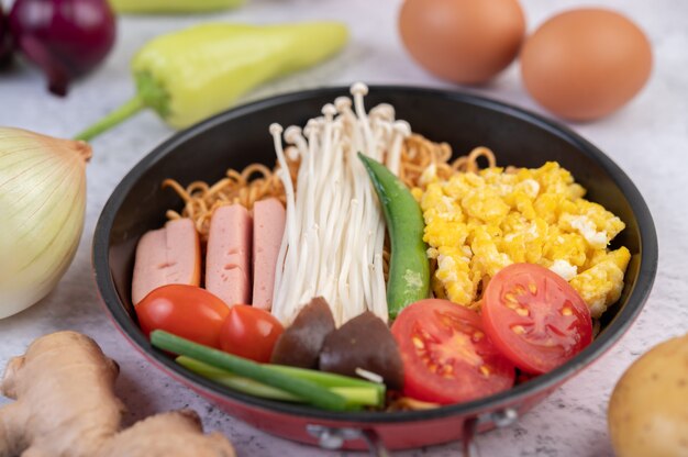 Fideos salteados que combinan maíz, setas con agujas doradas, tomate, salchichas, edamame y cebolletas en una sartén.