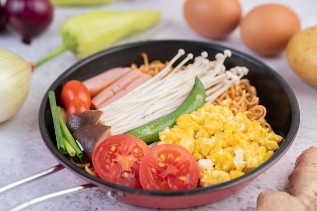 Fideos salteados que combinan maíz, setas con agujas doradas, tomate, salchichas, edamame y cebolletas en una sartén.