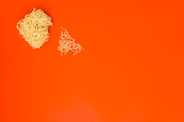 Fideos secos instantáneos rotos sobre fondo naranja