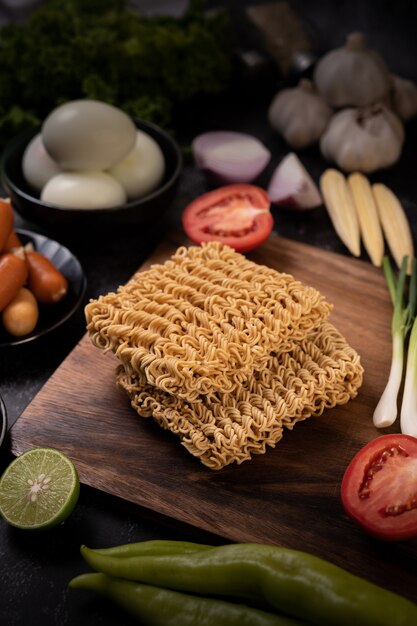 Fideos en una tabla de cortar de madera con tomate, lima, cebolleta, ají y maíz baby