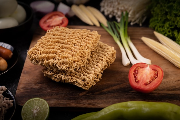 Fideos en una tabla de cortar de madera con tomate, lima, cebolleta, ají y maíz baby