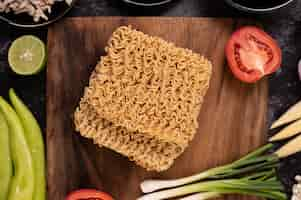 Foto gratuita fideos en una tabla de cortar de madera con tomate, lima, cebolleta, ají y maíz baby