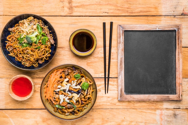 Fideos tailandeses tradicionales con salsa; palillos y pizarra en escritorio de madera