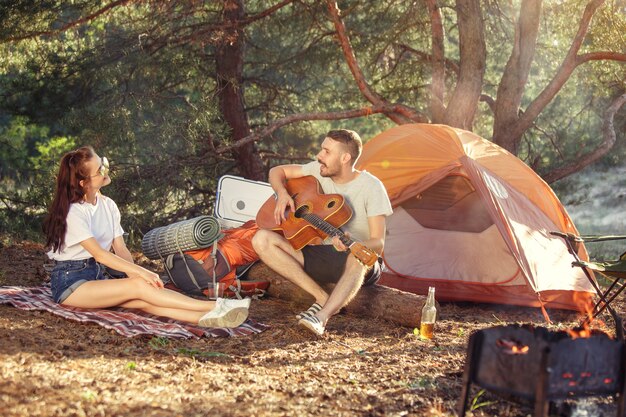 Fiesta, campamento de grupo de hombres y mujeres en el bosque. Se relajan, cantan una canción contra la hierba verde. concepto