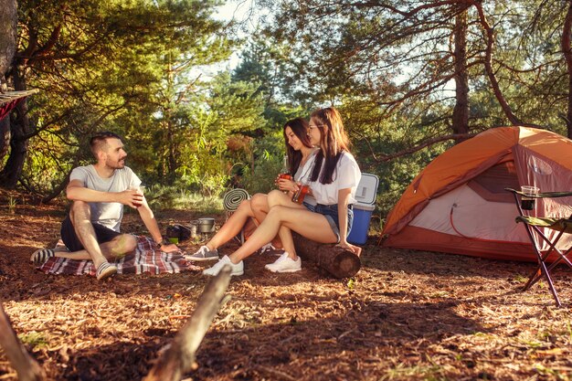 Fiesta, campamento de grupo de hombres y mujeres en el bosque. Se relajan contra la hierba verde. concepto