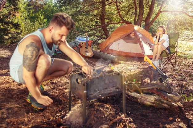 Fiesta, campamento de grupo de hombres y mujeres en el bosque. Se relajan contra la hierba verde. Las vacaciones, verano, aventura, estilo de vida, concepto de picnic.