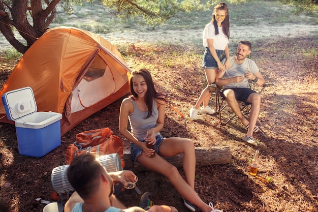 Foto gratuita fiesta, campamento de grupo de hombres y mujeres en el bosque. se relajan contra la hierba verde. las vacaciones, verano, aventura, estilo de vida, concepto de picnic.