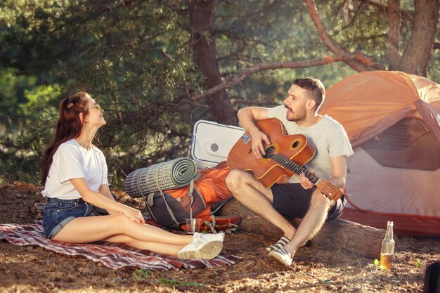 Fiesta, campamento de grupo de hombres y mujeres en el bosque. relajante, cantando una canción contra la hierba verde.